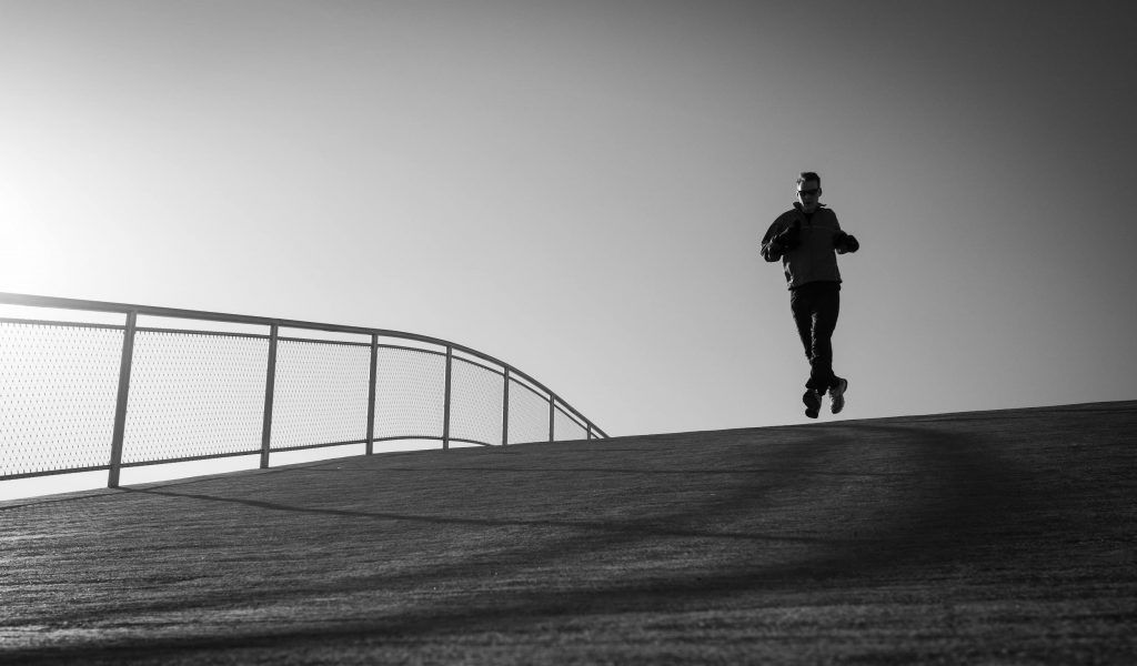 black-and-white-man-running-over-bridge